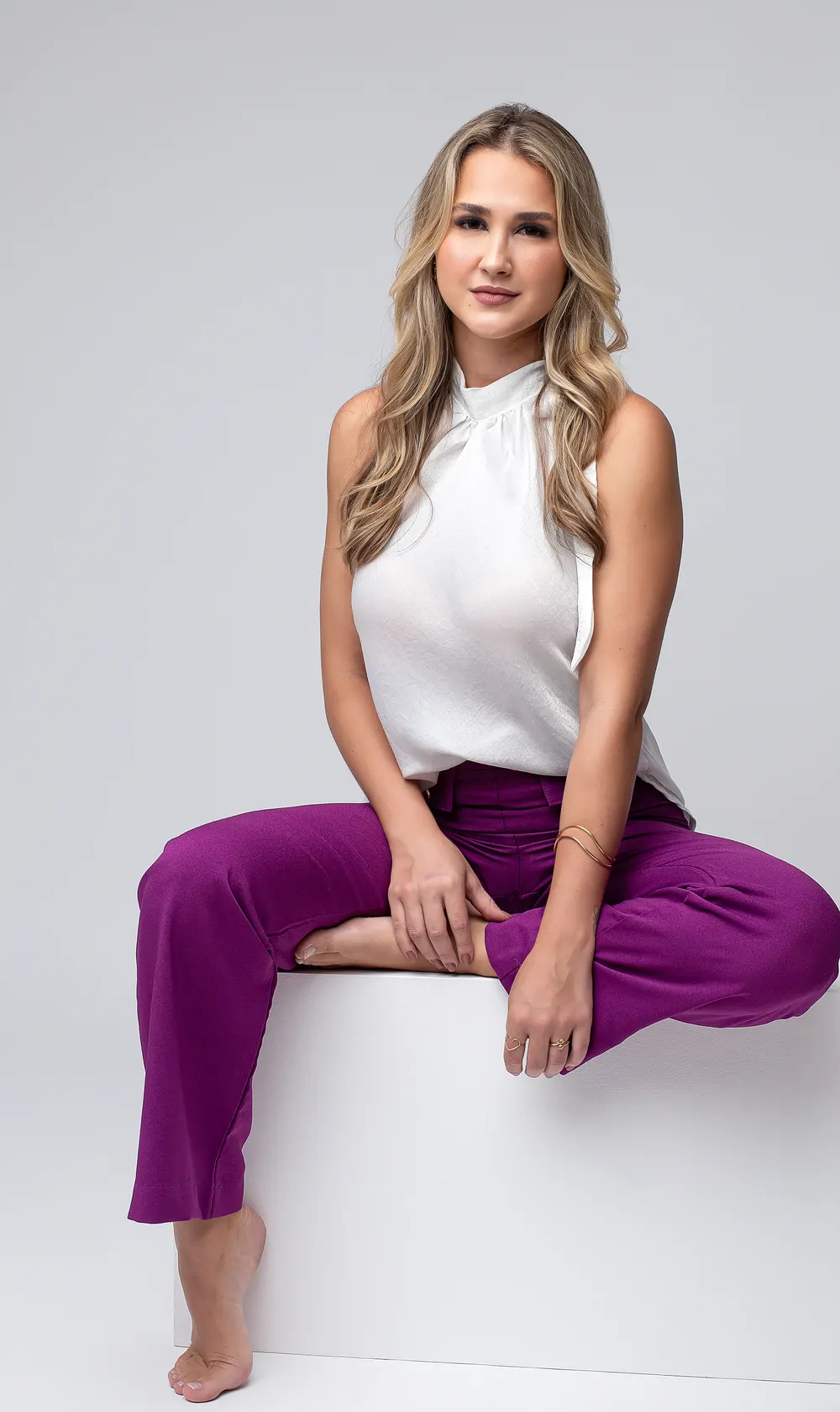 Sofia Schlemper Maciel sentada sobre um cubo branco, em estúdio de fundo claro.